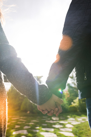 Young couple in love walking in the autumn park holding hands looking in the sunsetの写真素材