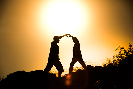 Silhouetted friend forming a heart symbol at golden hour sunsetの写真素材