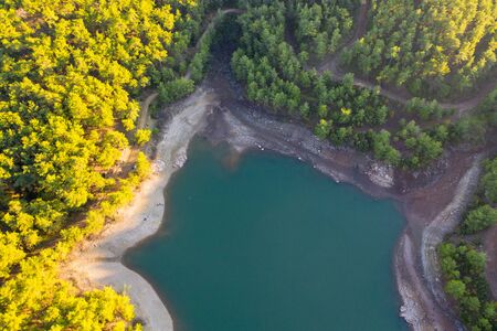 Natural ecological lake surrounded by pine trees between mountains near a village aerial photo.の写真素材