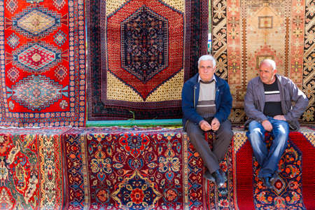 Two Armenian men sitting on the carpets at the Vernissage market in Yerevan, Armenia.