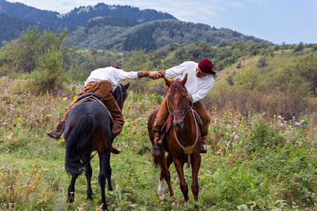 Kazakh men in national costumes performing traditional arm wrestling on horse known as Atpen...