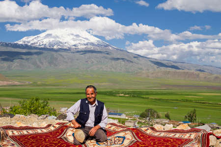 Kurdish man sitting on carpet, with the Mt Ararat in the background, in Dogubeyazit, Turkey.のeditorial素材