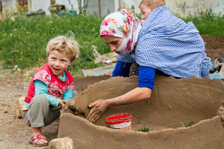 Kurdish woman carrying her baby on her back and works to make tandoor oven, in Diyarbakir, Turkey.のeditorial素材