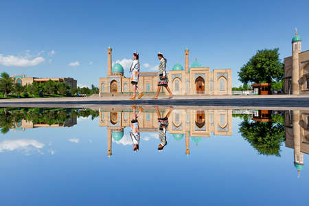 Reflection in puddle of water of the Khast Imam Mosque as girls walk in its courtyard, in Tashkent, Uzbekistan.のeditorial素材