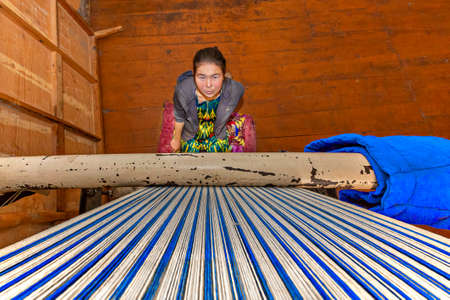 Local girl weaving rug and looking up the weaving loom, in Nukus, Uzbekistanのeditorial素材