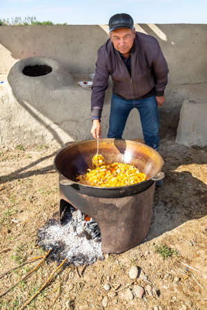 Uzbek man cooks vegetables in a big pot outdoors in the outskirts of Samarkand, Uzbekistanのeditorial素材