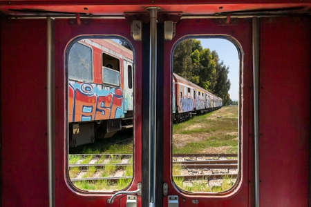 Abandoned train through the window on the door of another old train in Durres, Albania