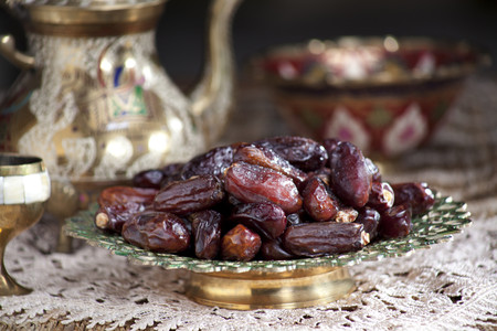 Close-up of an ornamental bowl of dried dates with kettle and glass on tablecloth