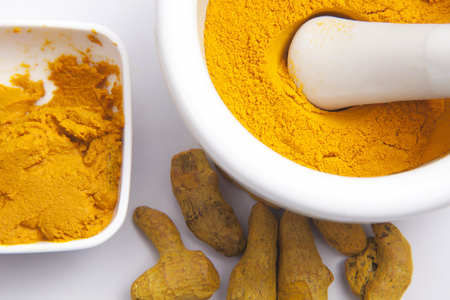 Turmeric powder in a mortar with Turmeric roots and paste isolated on white backgroundの写真素材