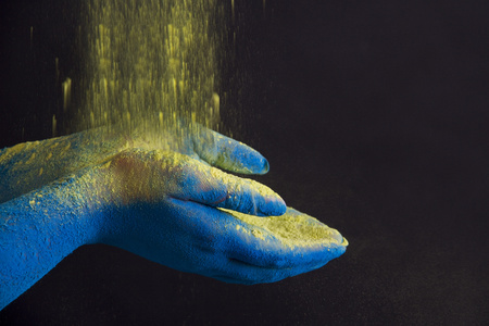 Yellow powder falling on blue cupped hands against black background
