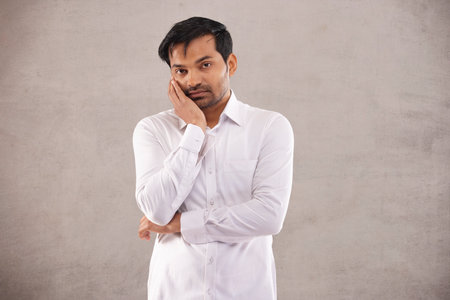 Portrait of a sad young man in white shirt looking at camera with his hand on cheek