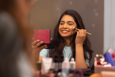 Young woman doing her make up in front of mirror