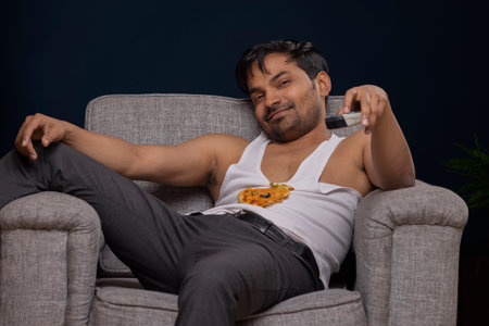 Portrait of an exhausted young man lying on sofa and watching televisionの写真素材