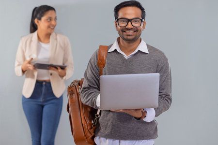 Young corporate employee standing with laptop and his colleague standing behind with digital tablet