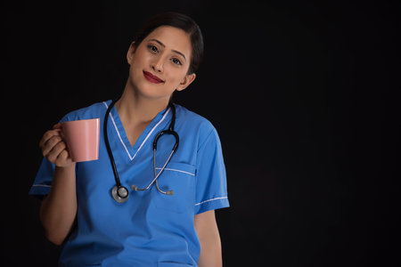 Portrait of a happy female nurse with a cup of coffee against dark backgroundの写真素材