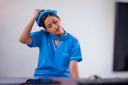 Portrait of a tired female nurse removing surgical cap while sitting at computer deskの写真素材