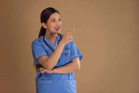 Portrait of a smiling female nurse pointing away with index finger against plain backgroundの写真素材
