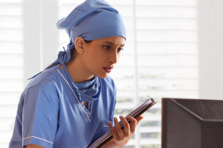 Close-up of female nurse holding clipboard and using computer in hospitalの写真素材