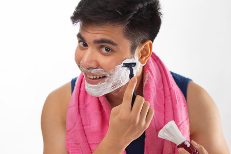 Close-up portrait of young man applying shaving cream to his face in bathroom at homeの写真素材