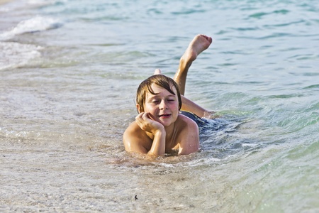 young boy enjoys lying at the beach in the surfの写真素材