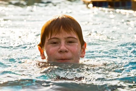 boy with red hair is swimming in the pool and enyoing the fresh water