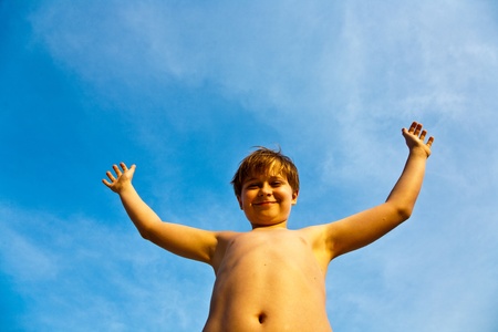 happy smiling young boy with background blue sky irises up his armsの写真素材