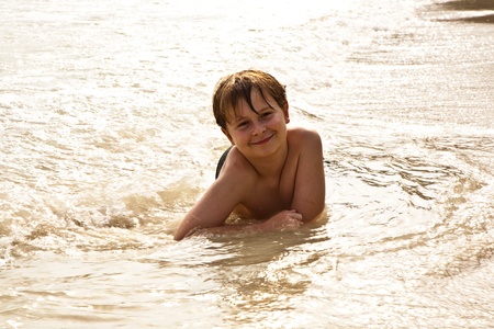 boy iy lying at the beach and enjoying the warmness of the water and looking self confident and happyの写真素材