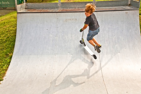 boy enjoys riding his scooter in the skate park