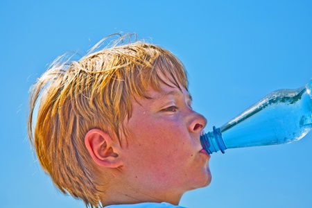young boy drinks water out of a bottle after sports