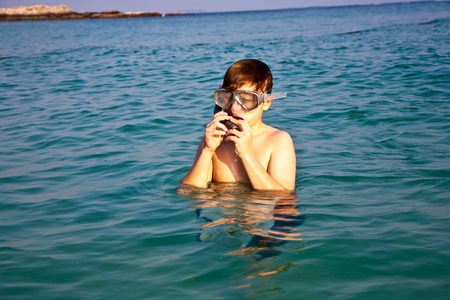 young boy is standing in the beautiful clear sea, enjoying the water and starts snorkelingの写真素材