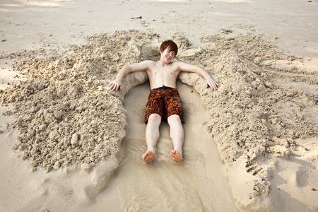 boy with red hair is lying in a sandy bed at the beauti ful beachの写真素材