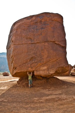 Monument Valley, child has fun by simulatings to carry a big rock with his hand just by leaning on it, near Spring Sandstone Formationの写真素材
