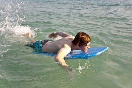 boy is surfing on a small surfboard on a beautiful sea with crystal clear water and blue skyの写真素材