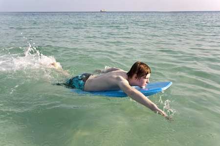 boy is surfing on a small surfboard in a beautiful sea with crystal clear water and blue skyの写真素材