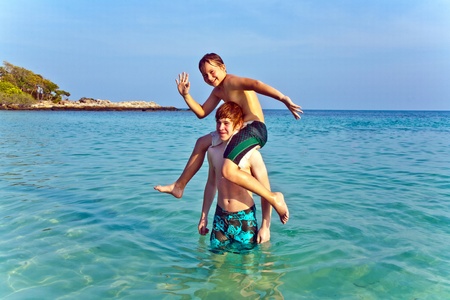 brothers are playing together in a beautiful sea with crystal clear water and blue skyの写真素材