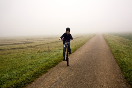 young boy on his mountain bike is on a bicycle tour along beautiful countryside in heavy fogの写真素材