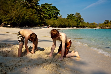 young boys are enjoying playing at the beach and building figures out of sand at the beautiful white beachの写真素材