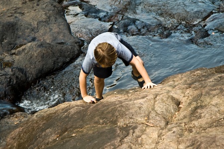 young boy climbing up a rockの写真素材