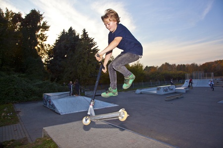 boy jumping with his scooter at the skatepark