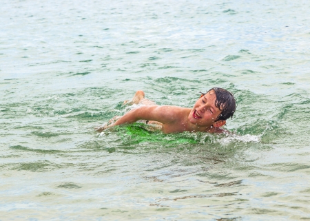 happy boy enjoys crawling in the ocean in the waves at the beachの写真素材