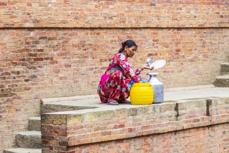 BHAKTAPUR, NEPAL- JUNE 16 : An unidentified Nepali woman fills up the water bottle with drinking water on June 16,2012 in Bhaktapur, Nepal. Bhaktapur is located about 20 km east of Kathmandu.のeditorial素材