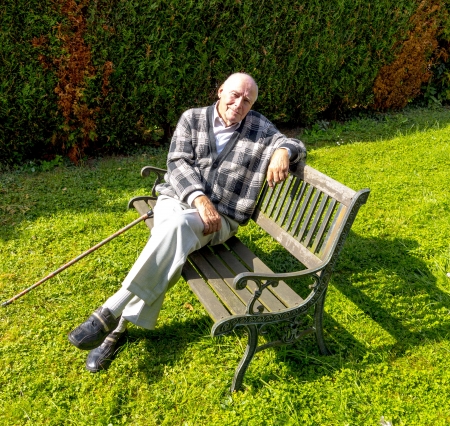 old man enjoys sitting on a bench in his gardenの写真素材