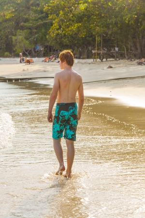 young boy is walking along the beautiful beach in backlightの写真素材