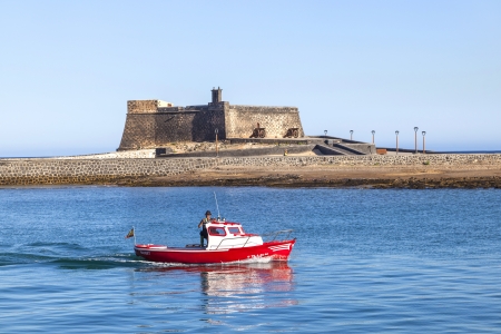 ARRECIFE, SPAIN - MARCH 29: fisherboat passing the castle Castillo de San Gabriel on March 29, 2013 in Arrecive, Spain. The Castillo was built in 1574 in order to defend Arrecife Harbour.のeditorial素材