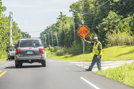 DAUPHIN ISLAND, USA - JULY 18, 2013: street worker shows slow sign to reduce speed at the construction site in Dauphin Island, USA.のeditorial素材