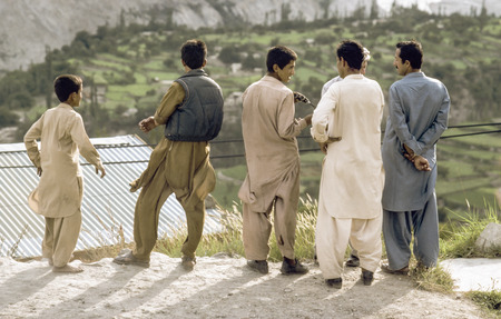 GILGIT, PAKISTAN - JUNE 30, 1987: pakistani men at Karakoram Highway in local dress watch the valley and discuss in Gilgit, Pakistan. The Karakoram Highway is the only street to china throuht wild mountain areas and valleys.のeditorial素材