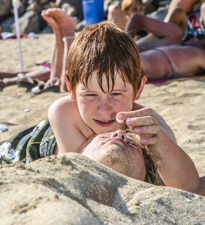 boy puts a white blossom on a girls nose at the beachの写真素材