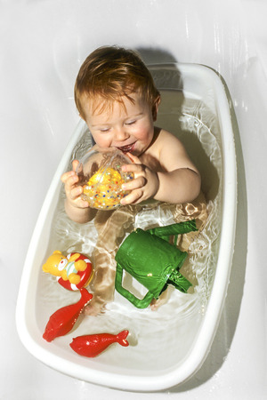 boy enjoys playing with the plastic toys in the bath tubeの写真素材