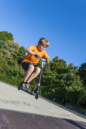boy has fun riding his push scooter at the skate parkの写真素材