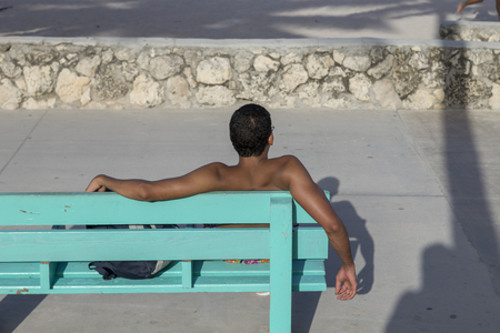 MIAMI, USA - AUG 18, 2014: man with suntan sits at a bench in south beach and enjoys the Miami sun.is the famous beach in Miami and the benches are all colored in light green.のeditorial素材